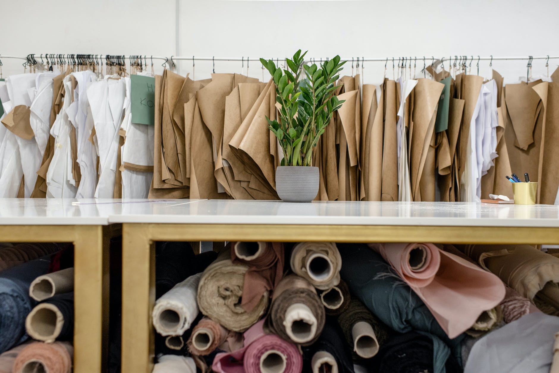 fashion studio with sewing patterns hanging on a rail, a long table and fabric rolls wedged underneath it